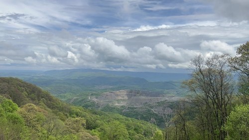 A panoramic view of lush green mountains under a cloudy sky, with a valley and distant hills in the background.