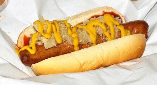 A hot dog in a bun topped with mustard and sauerkraut, served in a paper wrapper.
