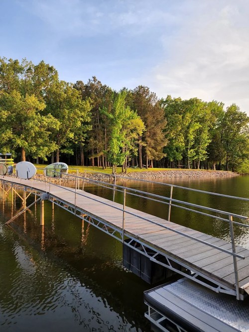 A wooden dock extends over calm water, surrounded by lush green trees and a serene landscape.
