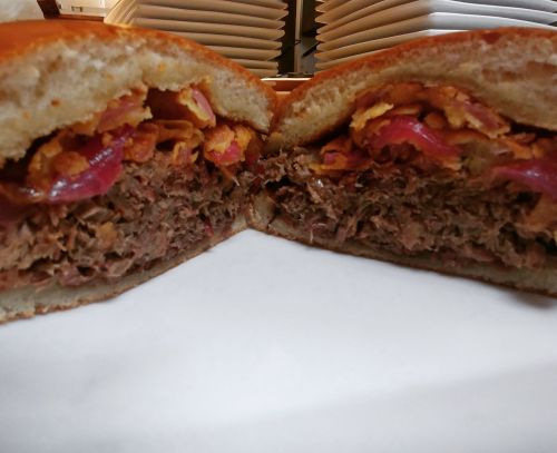 A close-up of a halved burger with shredded meat, crispy toppings, and pink onions on a soft bun.
