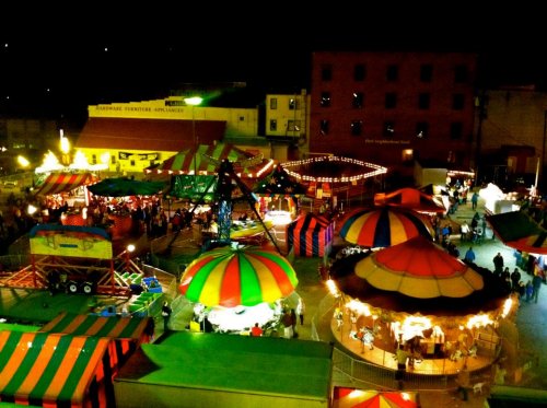 A vibrant night scene of a carnival with colorful tents, rides, and crowds enjoying the festivities.
