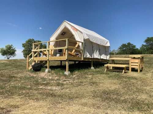 A glamping tent on a wooden platform, surrounded by grass and trees under a clear blue sky.