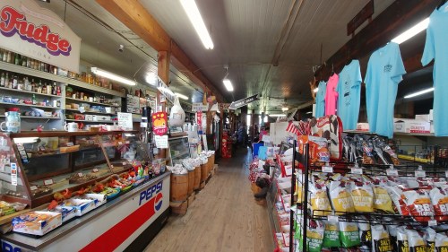 A wide view of a rustic general store aisle filled with snacks, drinks, and various goods on display.