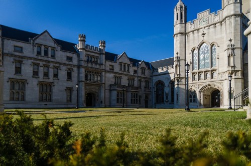 Historic stone buildings with intricate architecture, surrounded by green grass under a clear blue sky.