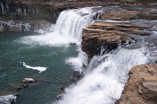 A scenic waterfall cascading over rocky cliffs into a turquoise pool, with icicles hanging nearby.
