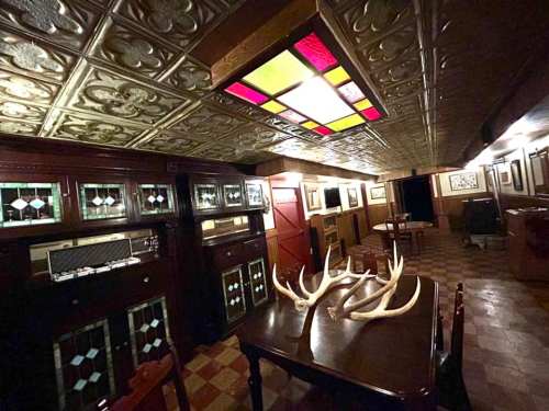 A dimly lit room with wooden furniture, antlers on a table, and ornate ceiling tiles, creating a rustic atmosphere.