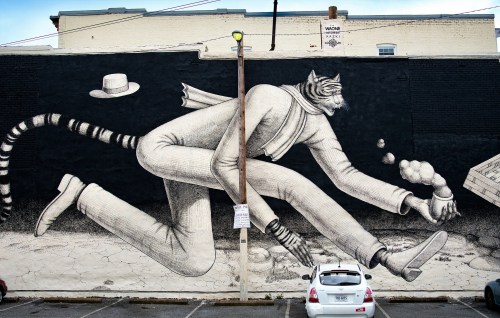 A large mural of a tiger in a suit running, juggling objects, with a hat floating above, set against a black wall.