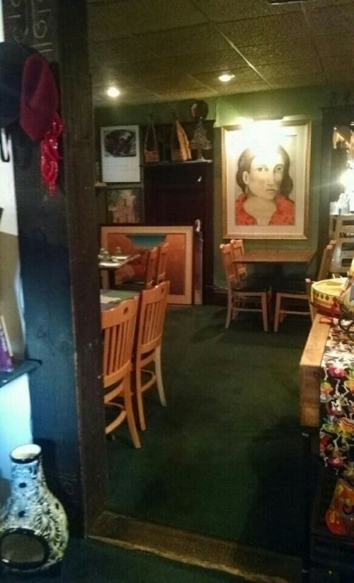 A cozy restaurant interior featuring wooden chairs, a large portrait on the wall, and decorative elements.