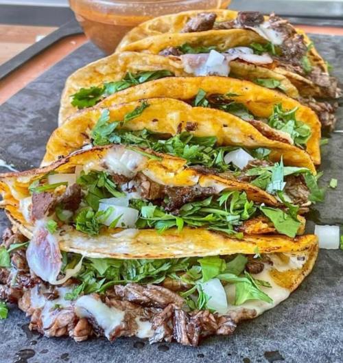 A close-up of stacked tacos filled with beef, onions, and fresh cilantro on a dark surface.