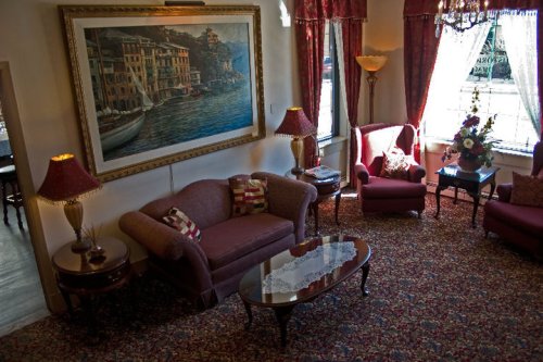 Cozy living room with a large painting, plush seating, decorative lamps, and floral arrangements. Warm, inviting atmosphere.