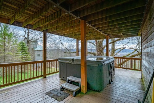 A wooden deck with a hot tub, surrounded by trees and a scenic view in the background.