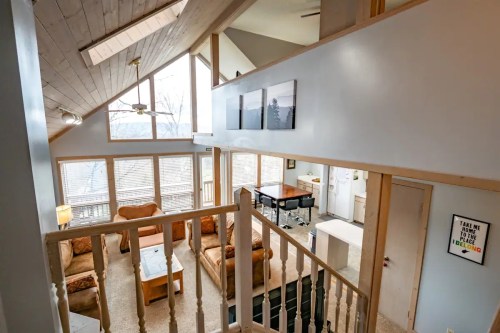 A spacious, modern living area with large windows, wooden beams, and cozy furniture, overlooking a scenic view.