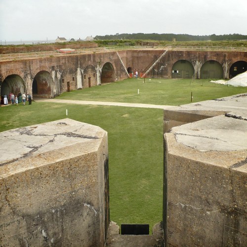 View of a historic fort's interior courtyard with brick arches, grassy areas, and visitors exploring the site.