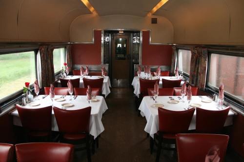 Interior of a vintage dining car with tables set for a meal, featuring red chairs and white tablecloths.