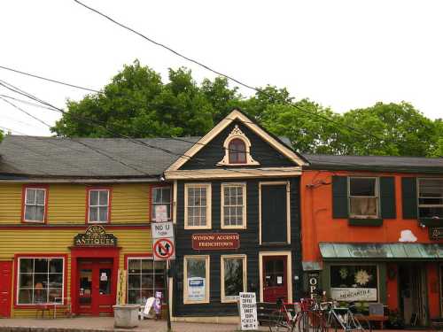 Colorful storefronts line a street, featuring a yellow building, a blue house with a decorative window, and an orange shop.