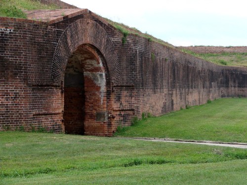 A brick archway in a historic fortification, surrounded by grassy terrain and a stone wall.
