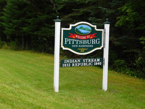 Welcome sign for Pittsburg, New Hampshire, featuring establishment dates and surrounded by greenery.