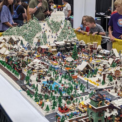 A detailed LEGO winter village scene with snowy mountains, trees, and people enjoying various activities.