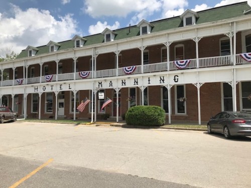 Historic Hotel Manning with a green roof, white railings, and patriotic decorations, set against a blue sky.