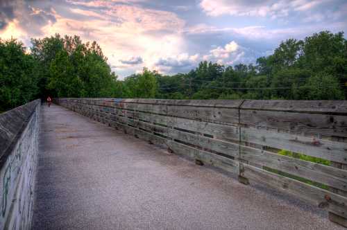 A wooden bridge stretches into the distance, surrounded by trees and a colorful sky at sunset.