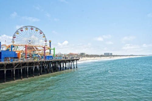 A vibrant pier with a Ferris wheel, overlooking a sandy beach and calm ocean under a clear blue sky.