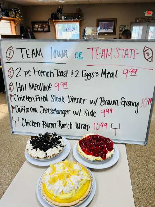 Menu board displaying food items and prices, including French toast, meatloaf, steak dinner, cheeseburger, and desserts.