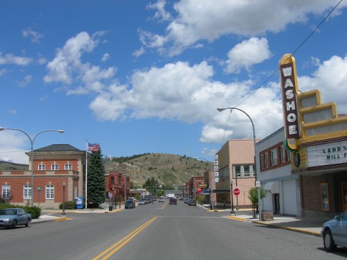 A small town street with buildings, a theater marquee, and mountains under a blue sky with fluffy clouds.
