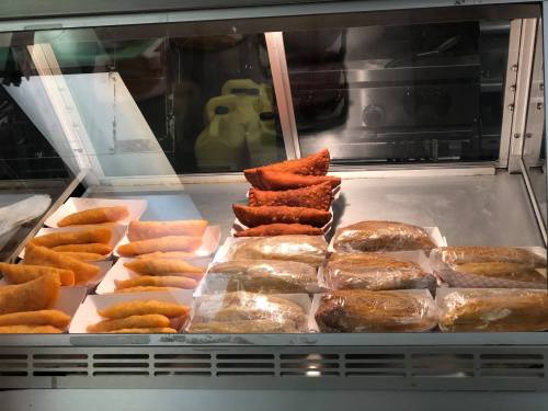 A display case filled with various types of fried pastries, including golden empanadas and stuffed pastries.