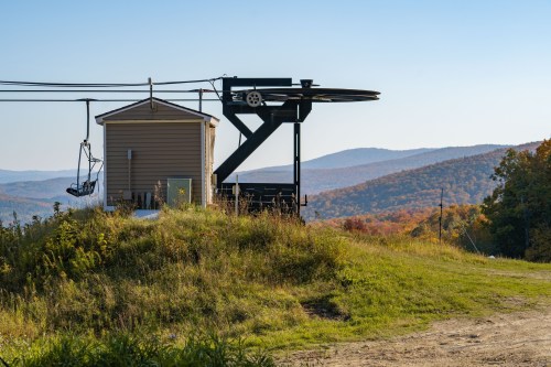 A ski lift station on a grassy hill with mountains in the background, showcasing autumn foliage under a clear sky.
