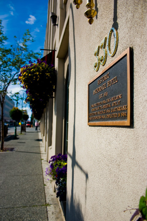Plaque on the Historic Anchorage Hotel, with flowers and a clear blue sky in the background.