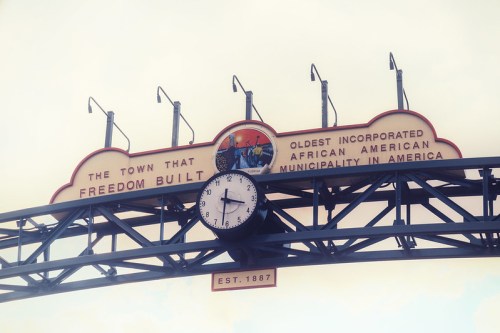 Sign reading "The Town That Freedom Built" with a clock, marking the oldest incorporated African American municipality, est. 1887.
