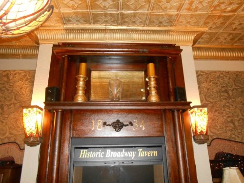 Interior of the Historic Broadway Tavern featuring a wooden mantel, decorative sconces, and a vintage ceiling.
