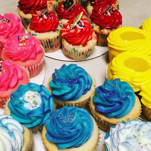A colorful assortment of cupcakes with pink, red, and blue frosting, topped with sprinkles and glitter.