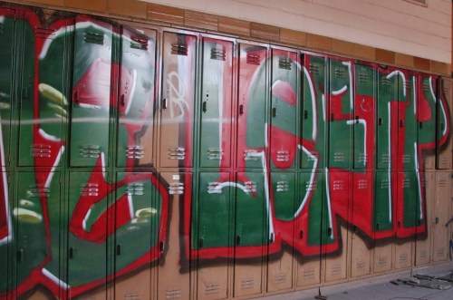 Colorful graffiti spelling "BLESSED" on a row of school lockers in a dimly lit hallway.
