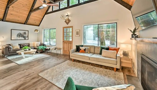Cozy living room with large windows, wooden beams, and modern furniture, featuring a mix of green and neutral tones.