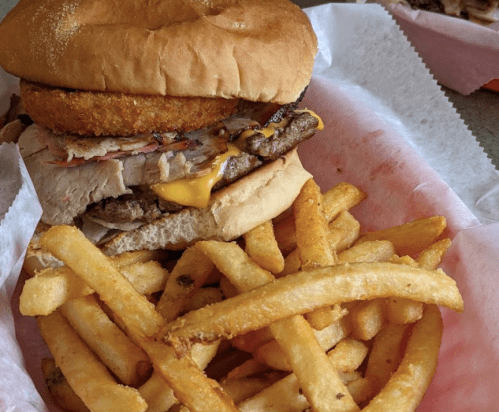 A hearty sandwich with layers of meat and cheese, served with a side of golden French fries in a basket.