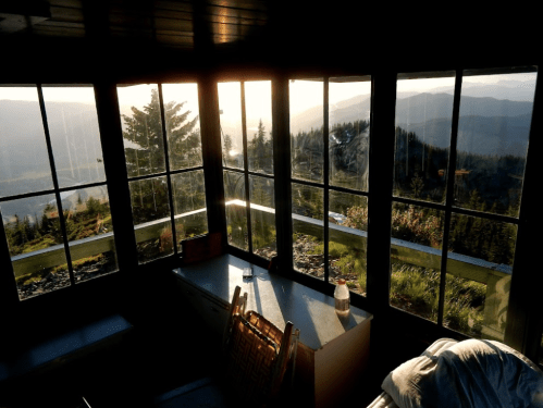 A cozy cabin interior with large windows showcasing a scenic mountain view at sunset.