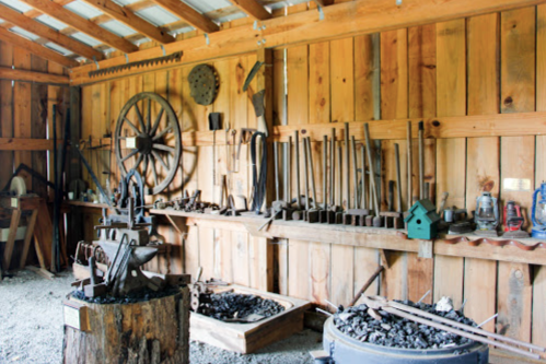 A rustic workshop with wooden walls, featuring tools, an anvil, and various metalworking equipment on display.