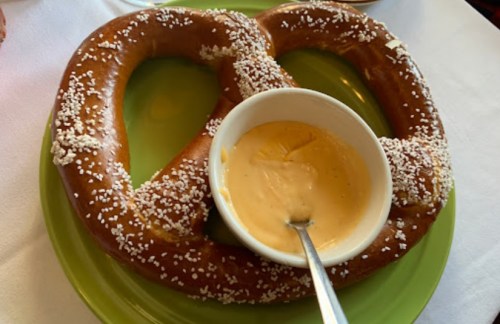 A large, soft pretzel with coarse salt served on a green plate alongside a small bowl of cheese dip.