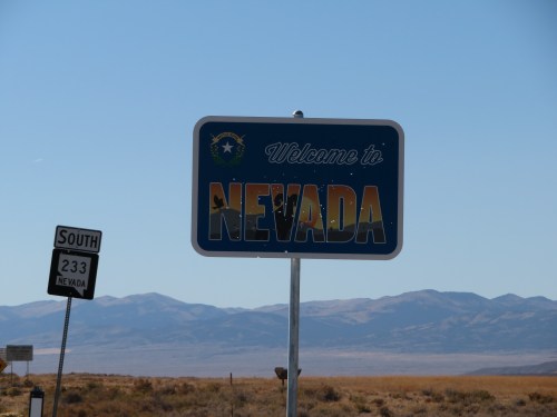 Welcome to Nevada sign with mountains in the background and a highway sign indicating South 233.