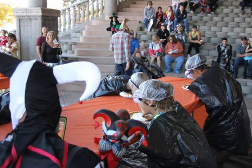 A group of people in costumes participate in a food-eating contest, while an audience watches from the steps.