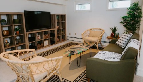 Cozy living room with a TV, rattan chairs, a green sofa, and decorative plants on a patterned rug.