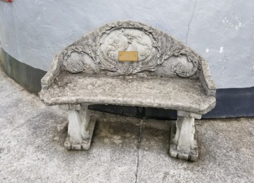 A weathered stone bench with ornate carvings, set against a gray wall.