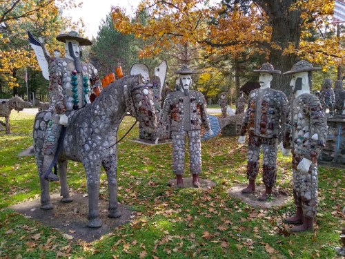 Stone sculptures of figures and a horse in a park, surrounded by autumn foliage and colorful leaves.