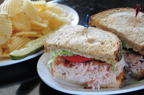 A sandwich with turkey, lettuce, and tomato, served with potato chips and a pickle on the side.