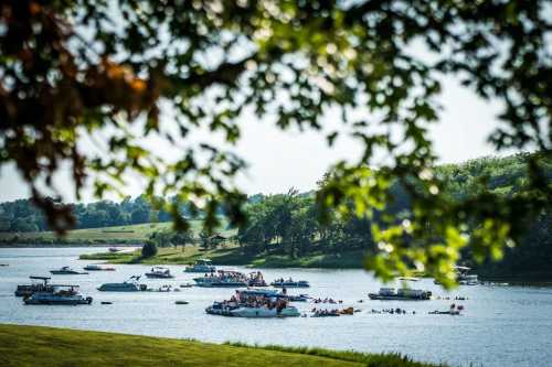 A scenic view of a lake filled with boats and people enjoying a sunny day, framed by green leaves.