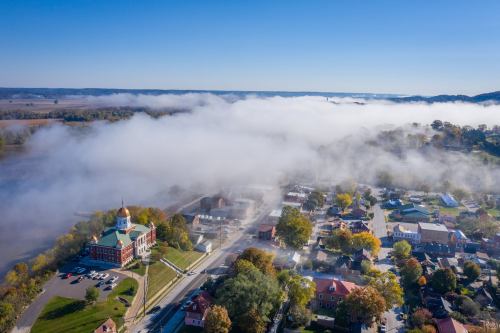 Aerial view of a town with fog rolling in, featuring a historic building and colorful autumn trees.