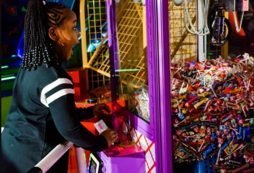 A child excitedly plays a claw machine filled with colorful candy at an arcade.