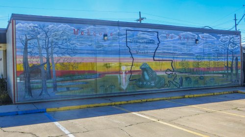 Mural depicting Louisiana landscape with trees, water, and a sunset, featuring the state outline and welcoming text.