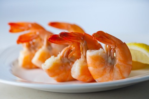 Three cooked shrimp on a white plate, garnished with a slice of lemon.